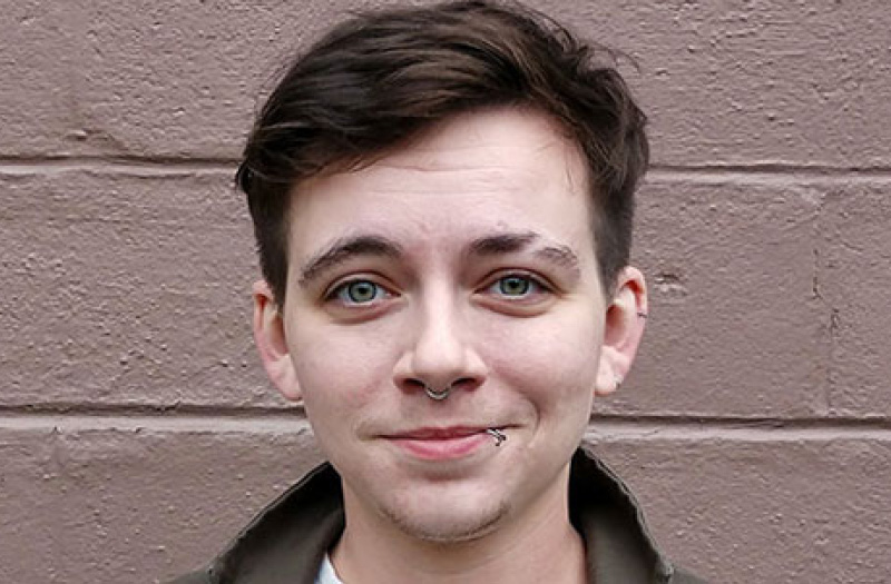 A closeup headfshot of a young man with a nose ring.